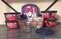 Lot of Pyrex glass storage bowls with lids, measuring cup, and additional containers shown on shelf.