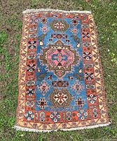 Full view of a small wool knotted rug with central medallion and border patterns laid on grass