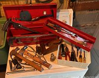 Full view of red metal toolbox with various hand tools including hammers, saws, screwdrivers, pliers, and wooden level laid out.