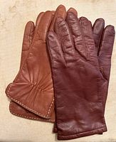 Two pairs of womens leather gloves, one brown with white decorative stitching and the other burgundy, shown side by side on a light background.