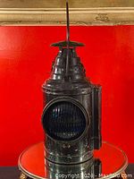 Full view of the antique railroad lantern showing its tapered vented top, large round lens, and handle.