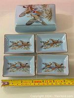 Rectangular porcelain box with lid and four small dishes, hand painted flying ducks and foliage on light blue background with gold trim. Measuring tape shows dishes about 4.5 inches long.