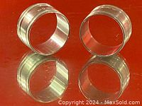 Two round silver napkin holders standing upright on a red surface, showing the polished reflective metal and detailed beaded edges.