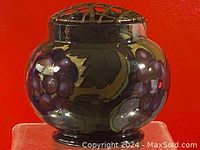 Front view of porcelain incense burner showing grape and leaf painted design with metal lattice lid against red background.