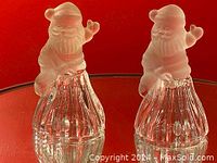 Two Santa glass bells with frosted glass Santas on clear ribbed glass bell bases shown against red background.