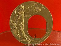 Close-up of the solid brass circular picture frame with detailed female figure relief and wreath, set against red background.