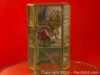 Full view of the vintage glass curio cabinet showing stained glass floral and butterfly panels on the shelves and sides, framed in brass or gold-tone metal.