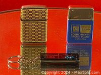 Photo shows two vintage metal lighters and a black keychain with a small folding knife on a reflective surface.