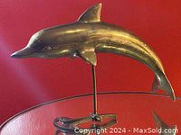 Front view of the vintage solid brass dolphin figurine on glass surface with red background.
