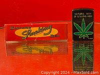 Photo of black Zippo lighter with cannabis leaf and text 'Natures Way of Staying High' alongside a pack of Smoking King Size Red rolling papers.