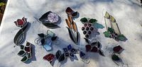 Photo showing 11 various flower-themed and decorative stained glass style suncatchers laid out on a white surface with colorful glass and metal edging.