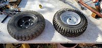 Two tires on metal rims displayed on a table outdoors.