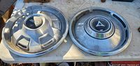 Photo of two hub caps front side, one with distinctive 'A' emblem and chrome finish.