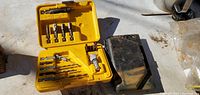 Photo showing two smaller tool kits, a yellow plastic tool case with multiple drill bits and attachments, and a black tool case with more tools inside, placed on a surface.