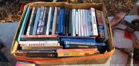 Cardboard box filled with assorted DVD movies without plastic cases.