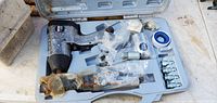 Craftsman pneumatic air impact wrench, air hammer, multiple air hose fittings, and blue Teflon tape inside hard plastic carrying case. Tools show signs of surface rust and usage wear.