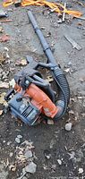 Side angle of Husqvarna backpack leaf blower showing orange blower housing and black intake tube.