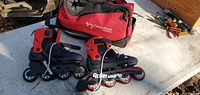 Side view of pair of Rollerblade inline skates with branded carry bag. Skates are black and red with four wheels each.