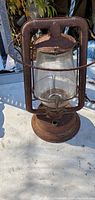 Photo showing rusty vintage brown metal lantern with clear glass globe, front view.