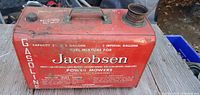 Side view of red metal gas can with painted white text showing capacity and fuel mixture instructions for Jacobsen power mowers.