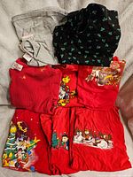 Nine Christmas-themed tops including Disney and Peanuts characters, folded and laid out on a light surface.
