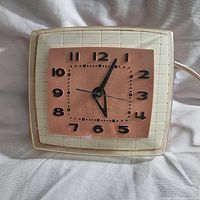 Front view of mid century GE Telechron electric clock showing pink face and black numerals with white grid frame.