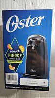 Photo of the Oster Electric Can Opener box showing the product image and feature of Power Pierce cutting blade.