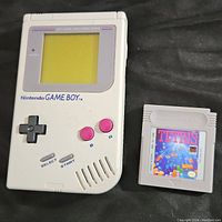 Front view of Nintendo Game Boy console with Tetris cartridge beside it on black fabric.