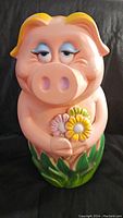 Front view of piggy coin bank holding flowers, showing face, flowers, and grass base.