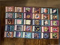 Overhead photo of 50 YuGiOh! 1st edition cards laid out with visible artwork on monster, spell, and trap cards showing various characters and spell graphics.