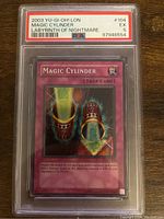 Front side of Magic Cylinder Yu-Gi-Oh! card from 2003, showing card name, effect and artwork inside a PSA graded protective case with grade 5 label visible.
