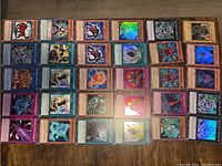 Photo showing 40 YuGiOh! trading cards arranged in 5 rows and 8 columns on a brown surface. Various monster cards with some holographic foiling, including dark and mechanical themes.
