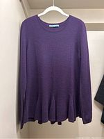 Front view of purple cashmere sweater hanging on white hanger showing round neckline, long sleeves, and ruffled hem