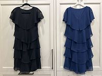 Front view of both dresses hanging side by side showing black and blue tiered layered flounce design and flutter sleeves.