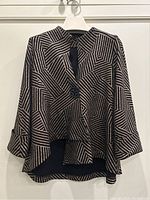 Full view of black jacket with gold geometric pattern hanging on white hanger; shows front button closure and asymmetrical hem.