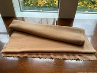 Folded camel-colored scarf on wooden table by window, showing overall appearance