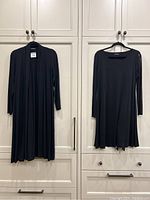 Two black Eileen Fisher garments hanging: a long open-front cardigan and a scoop neck long sleeve dress, both size medium.