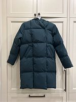 Front view of long forest green hooded puffer coat hanging on a hook