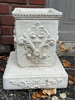 Front and side view of the square cement plinth base showing decorative carvings and textured edges.