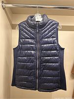 Front view of navy blue quilted puffer vest on hanger showing full body and front zipper.