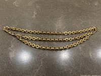 Full view of gold chain belt laid flat, showing the chain links and length.
