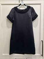 Full front view of black short sleeve beaded cocktail dress hanging on hanger on door.