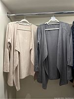 Two Gretchen Scott ultra suede cardigans hanging on a rack, one cream and one grey.