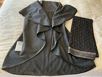 Full view of grey wool vest and folded black silk scarf on light background, showing vest's draped style and scarf's pattern.