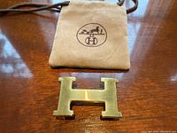 Front view of gold-tone brass H buckle and tan suede dust bag