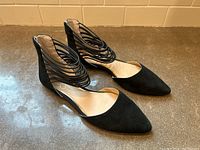 Side angle of black suede-like pointed flat shoes with looped strap ankle design.