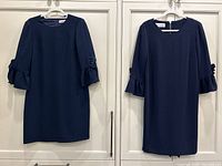 Front view of both navy blue cocktail dresses hanging side by side on white hangers showing sleeve designs and overall dress shape