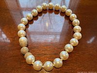 Full view of choker laid on wooden surface showing uniform large cream-coloured pearls and three gold-tone textured beads