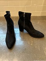 Front angled view of black suede ankle boots showing pointed toe, block heels, and side zippers.