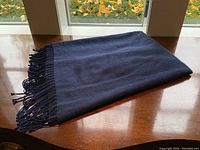 Folded shawl on wooden table under window showing overall appearance and color